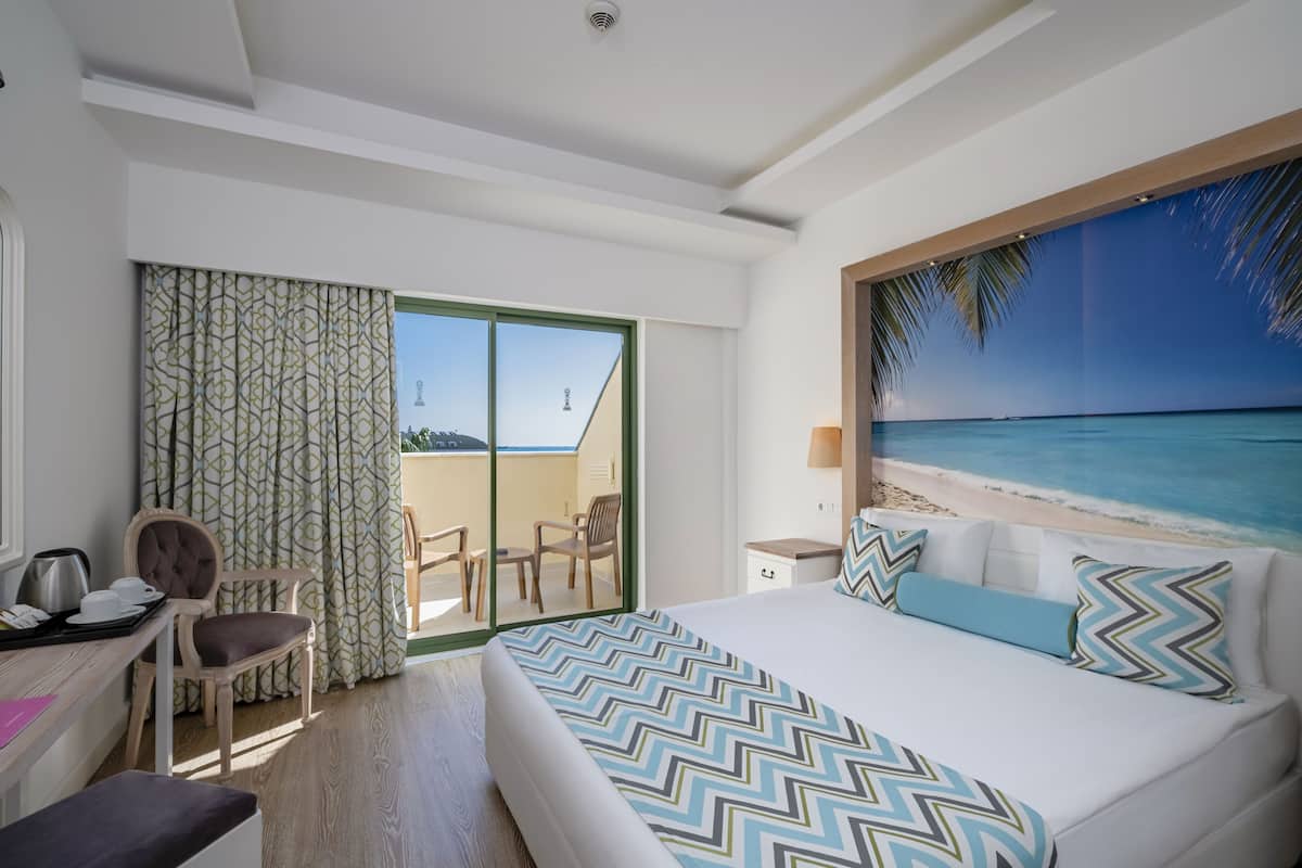 A hotel room with a bed, a desk, a chair, and a view of the beach.