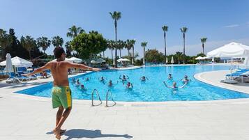 A swimming pool area with multiple pools, lounge chairs, and palm trees.