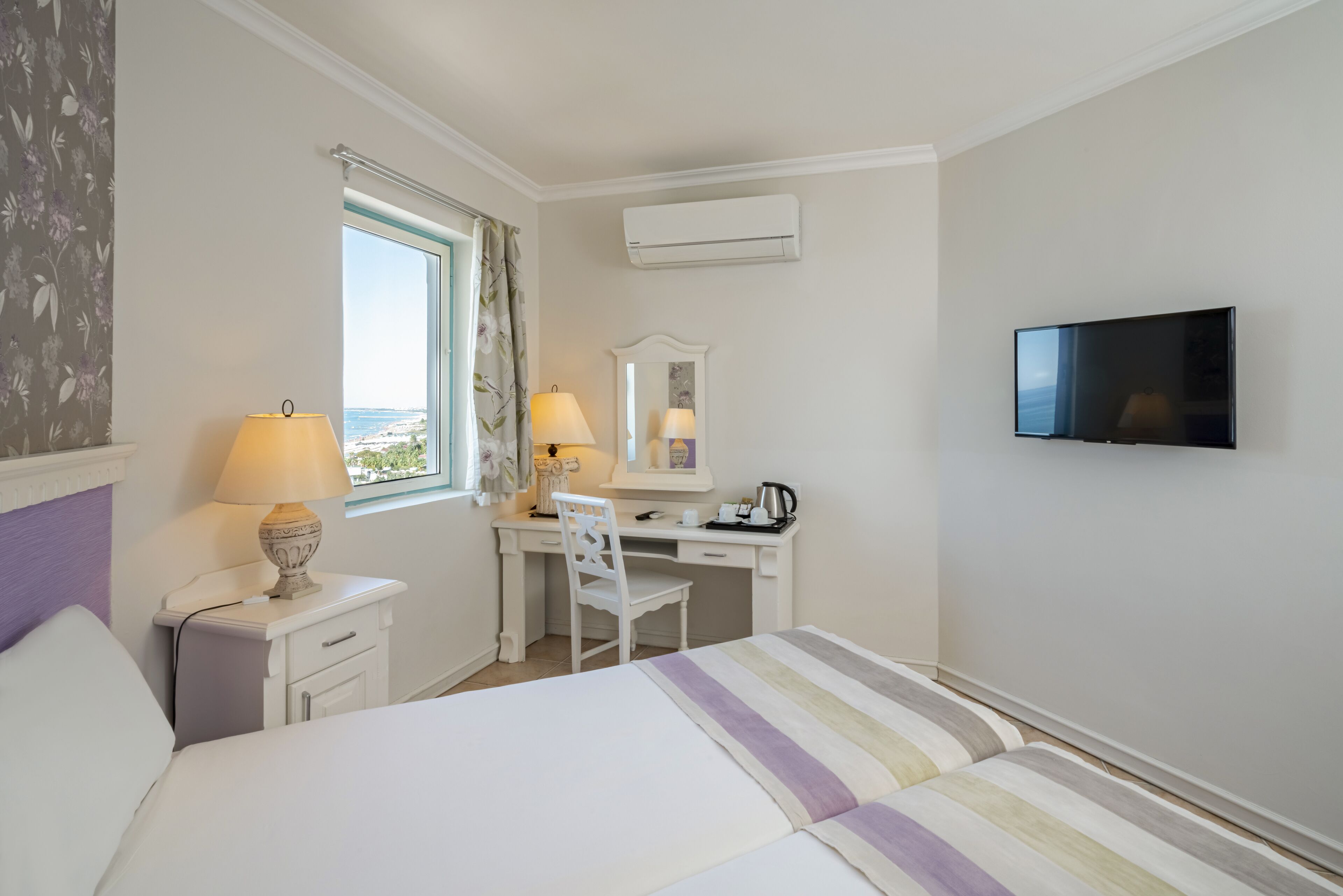 A hotel room with a bed, desk, chair, TV, and window with curtains.