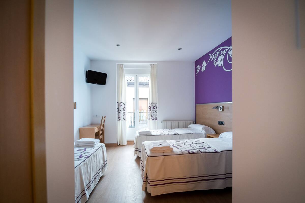 A hotel room with two beds, a television mounted on the wall, and a window with curtains.