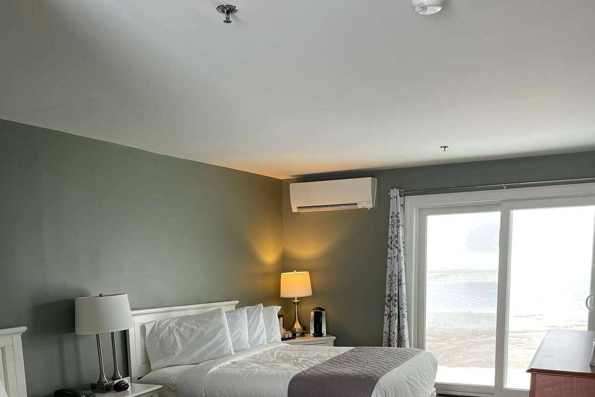 Habitación de hotel con dos camas, una mesita de noche con lámpara, unidad de aire acondicionado y vistas al exterior.