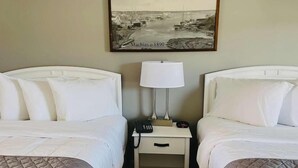 A hotel room with two beds, a nightstand with a lamp, a phone, and a framed picture of a harbor scene.
