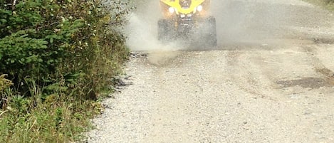 A person riding a yellow ATV on a gravel road surrounded by greenery.