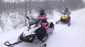Two snowmobiles on a snowy path with trees on either side.