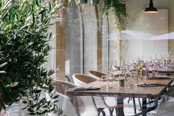 Un comedor con una larga mesa dispuesta para una comida, sillas y plantas colgantes.