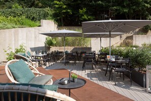 Une terrasse extérieure aménagée avec des meubles en osier, des parasols et un espace barbecue.