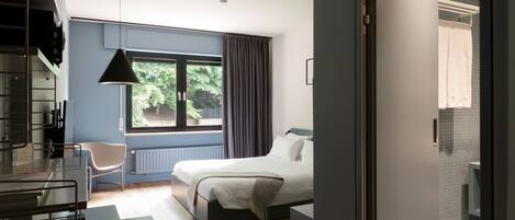 Una habitación de hotel moderna con una cama, un escritorio con silla, un ventanal con cortinas y vistas al exterior.