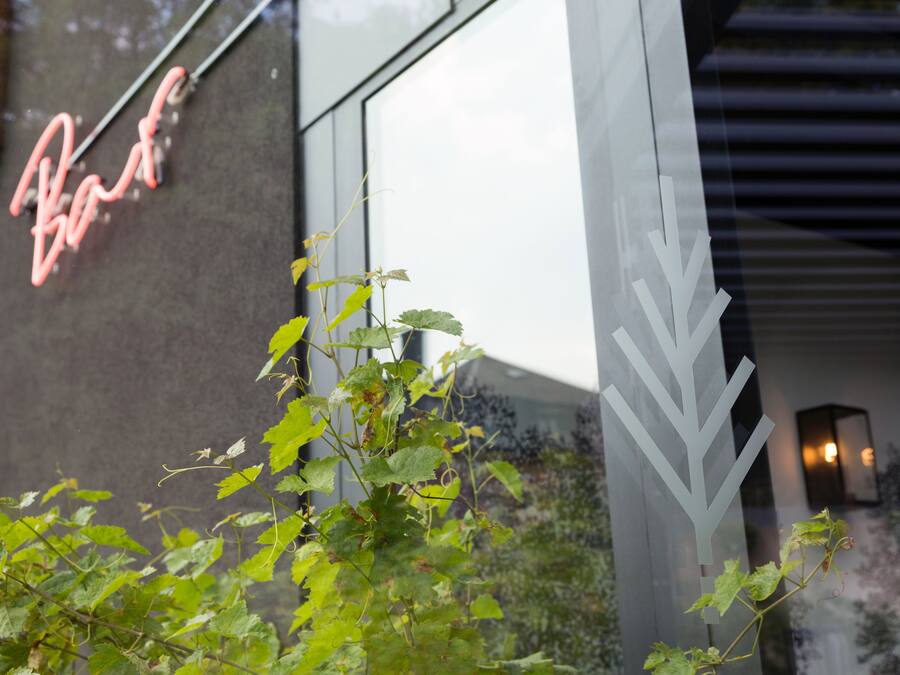 A building facade with a neon sign reading "Bar" and a modern architectural design with a glass window and a decorative white structure.