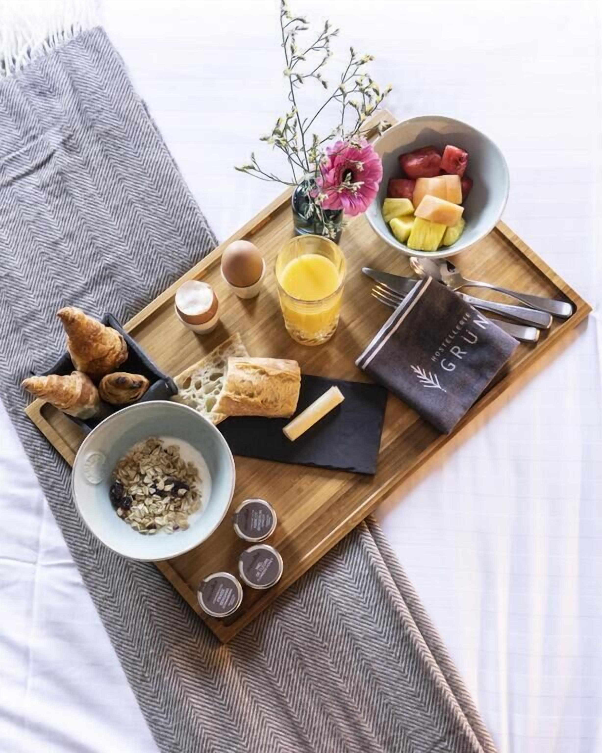 Bandeja de desayuno con cruasanes, un tazón de cereal, un vaso de jugo de naranja, un pequeño florero con flores y una fuente de fruta.
