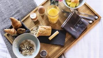 Bandeja de desayuno con cruasanes, un tazón de cereal, un vaso de jugo de naranja, un pequeño florero con flores y una fuente de fruta.