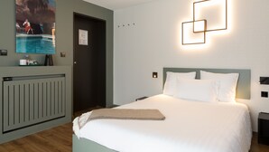 Una habitación de hotel ordenada con una cama grande, una obra de arte colgada en la pared, un radiador y una lámpara moderna.