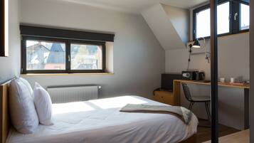 Un dormitorio con una cama, un escritorio, una silla, un radiador y una ventana.