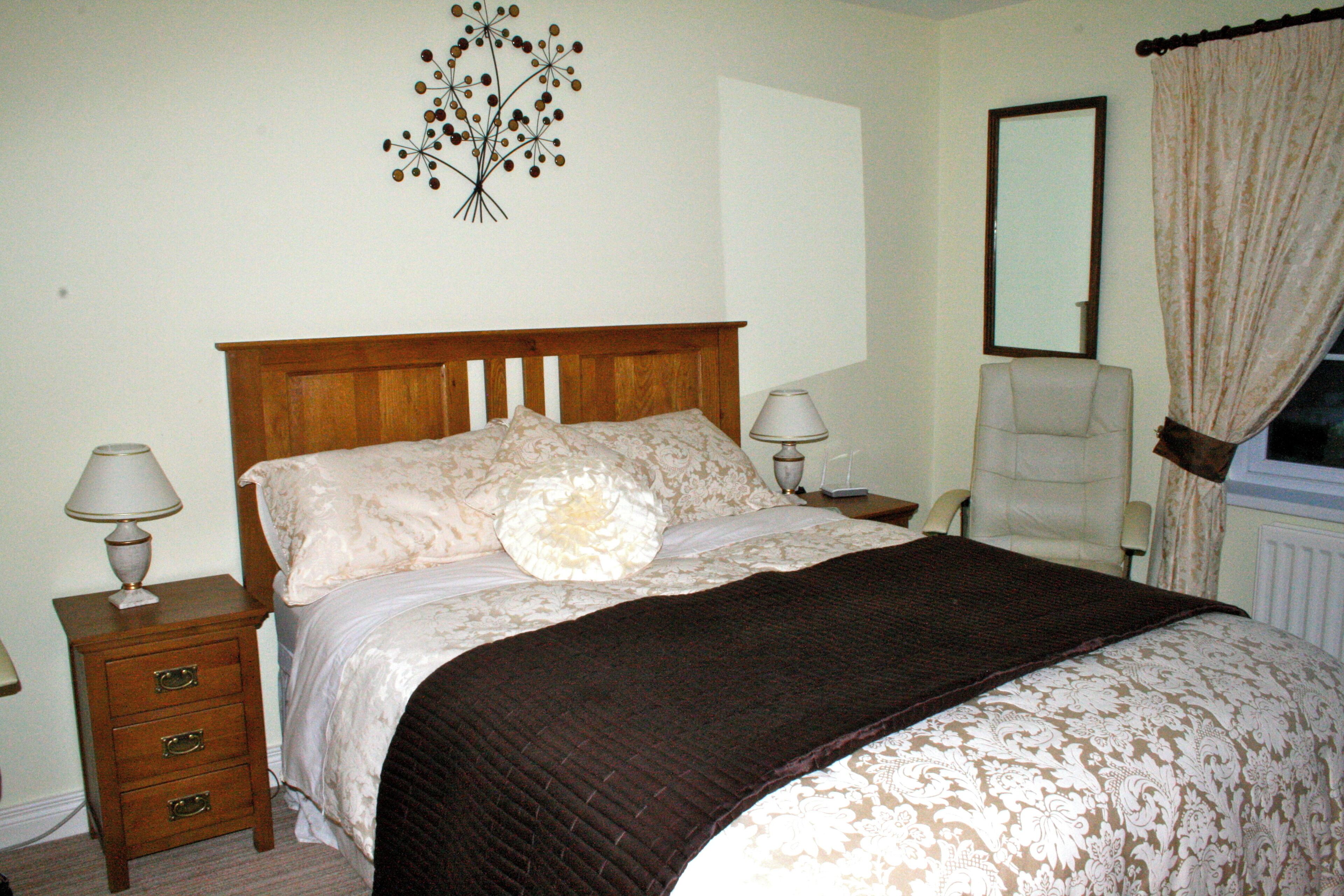 Un dormitorio con una cama de madera, dos lámparas de noche, una silla, un espejo y un adorno en la pared.