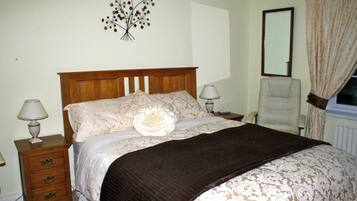 A bedroom with a wooden bed, two bedside lamps, a chair, a mirror, and a wall decoration.