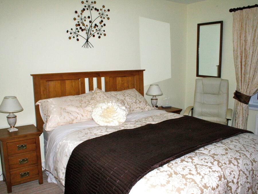 A bedroom with a wooden bed, two bedside lamps, a chair, a mirror, and a wall decoration.