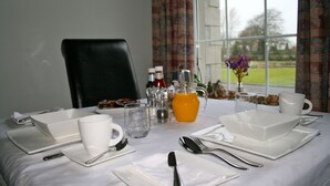 A neatly set breakfast table with white plates, bowls, and cutlery, a pitcher of orange juice, and a vase with flowers. - Ballyharvey House B&B (Antrim)