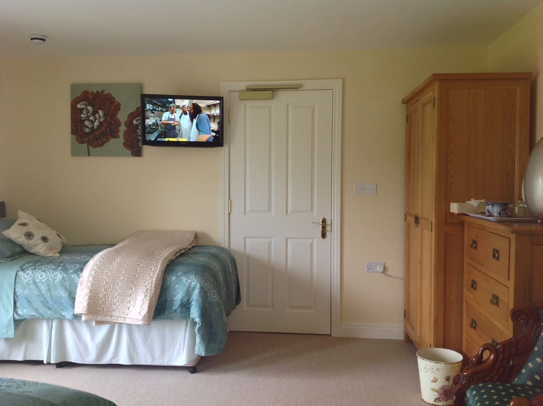 A bedroom with a bed, a television mounted on the wall, a wooden cabinet, and a door.
