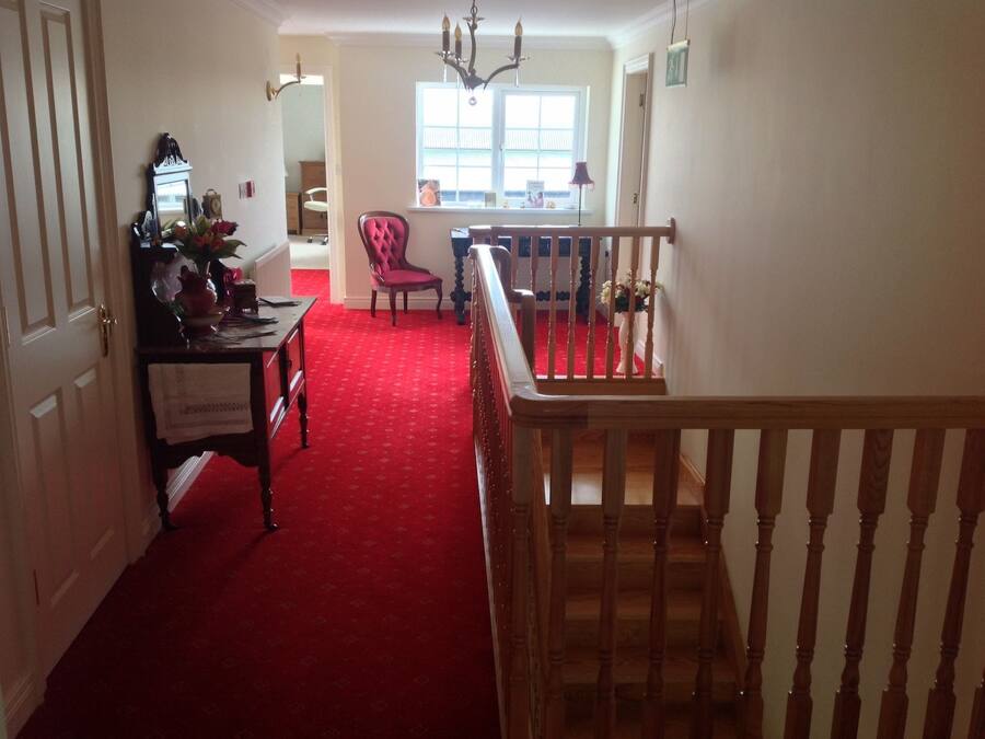 Un couloir recouvert d’une moquette rouge menant à un escalier doté d’une rampe en bois.