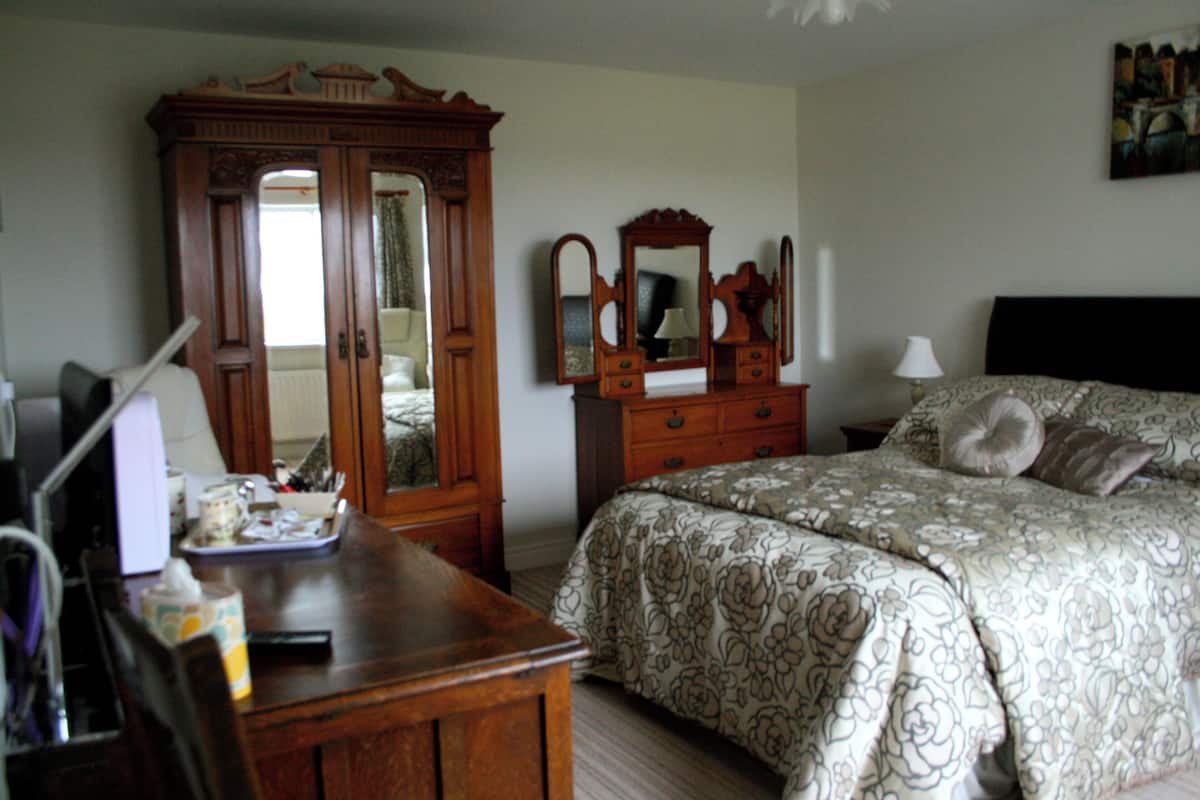 Une chambre à coucher avec un lit, une commode, un miroir, une lampe et un tableau accroché au mur.