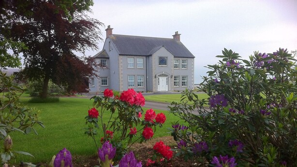 A large house with a grey roof and white walls, surrounded by a well-maintained lawn and flowering plants. - Ballyharvey House B&B (Antrim)