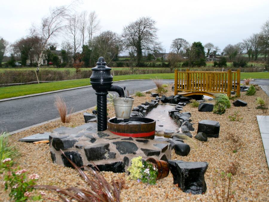 A garden with a stone fountain, a wooden bench, and a gravel path.