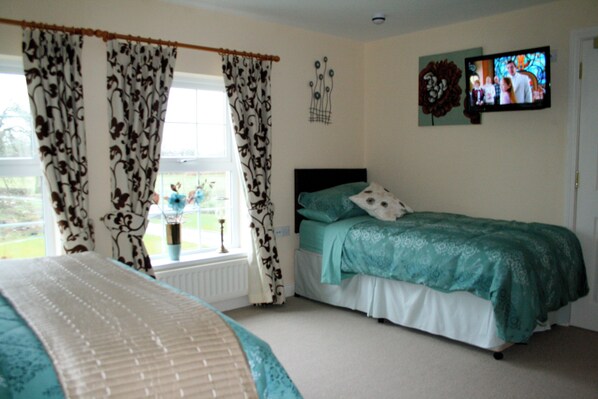 A bedroom with a bed, curtains, a window, and a television on the wall. - Ballyharvey House B&B (Antrim)