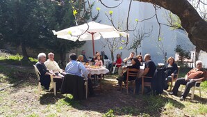 Un gruppo di persone sedute attorno a un tavolo sotto un ombrello, all'aperto in un giardino.
