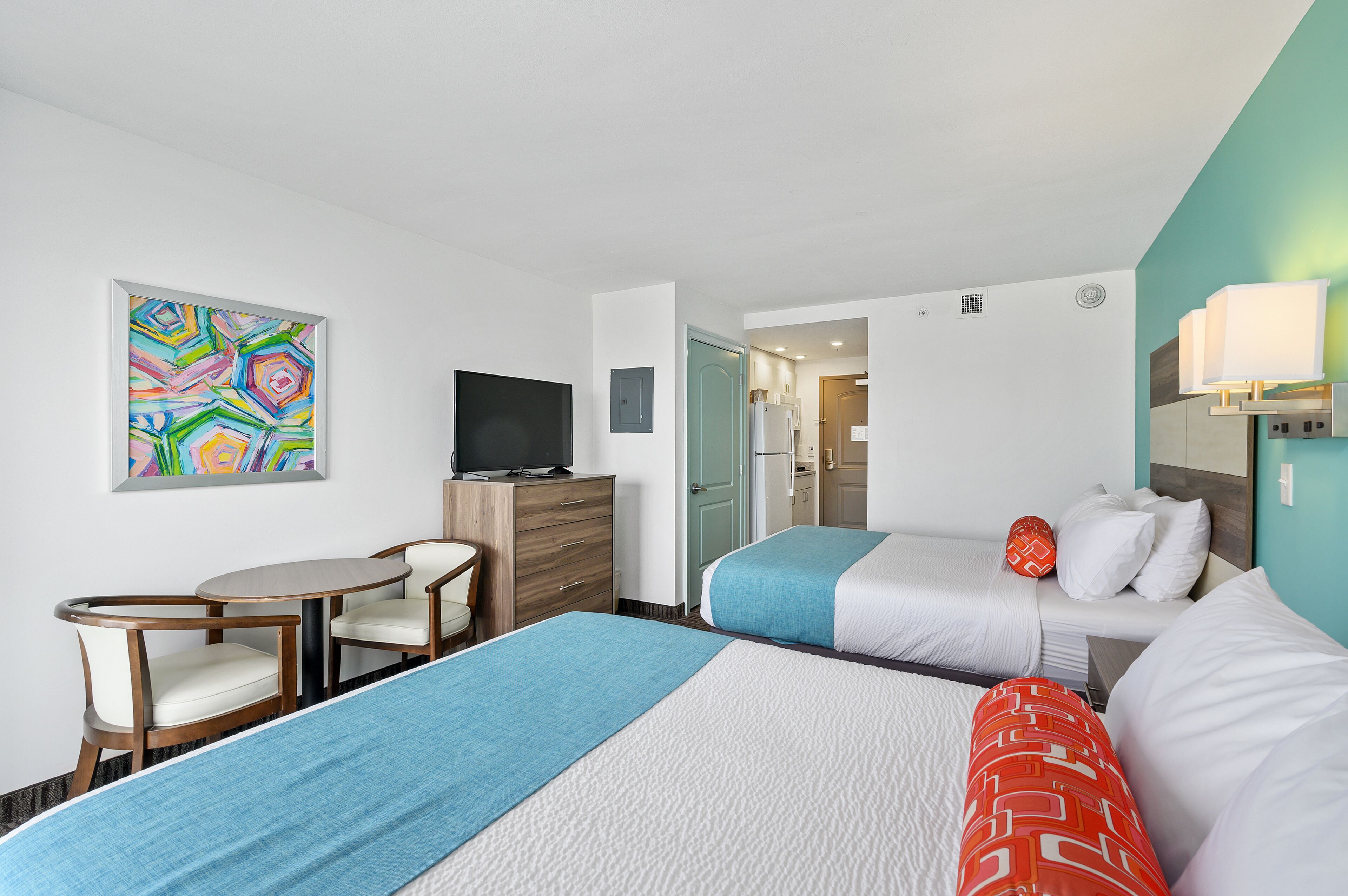 A hotel room with two beds, a desk, a chair, a television, and a colorful abstract painting on the wall.