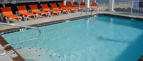 Un espace piscine avec un indicateur de profondeur de 3 pieds, des chaises longues orange et une vue sur la plage.