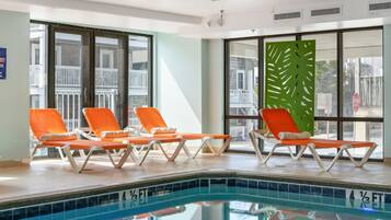Zona de piscina con cuatro sillones reclinables color naranja y un panel decorativo verde.