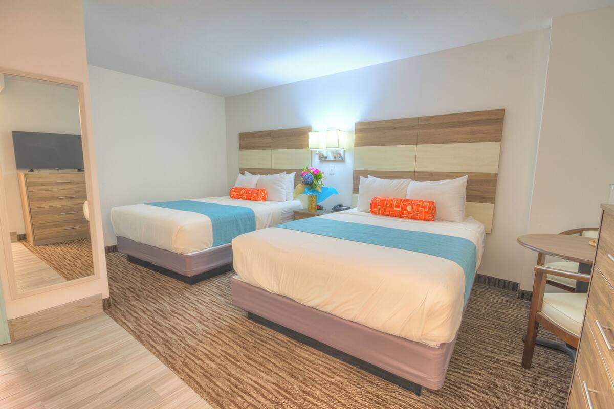 Une chambre d’hôtel avec deux lits, une petite table, une commode et un miroir.