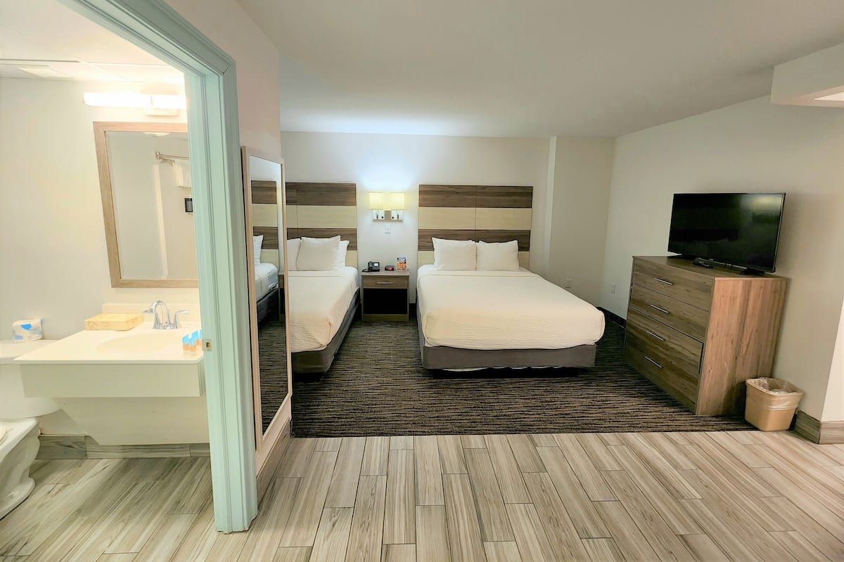Une chambre d’hôtel avec un grand lit, une télévision, une commode, une table de chevet et une salle de bain équipée d’un lavabo et d’un miroir.