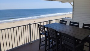Un espace extérieur abrité, doté d’une table et de chaises, qui offre une vue sur une plage, l’océan et un ciel dégagé.