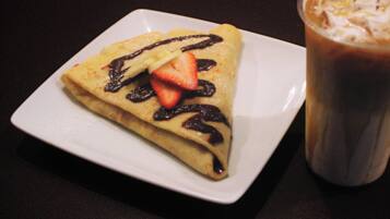 A square plate with a folded crepe topped with chocolate and a strawberry, and a glass of iced coffee beside it.