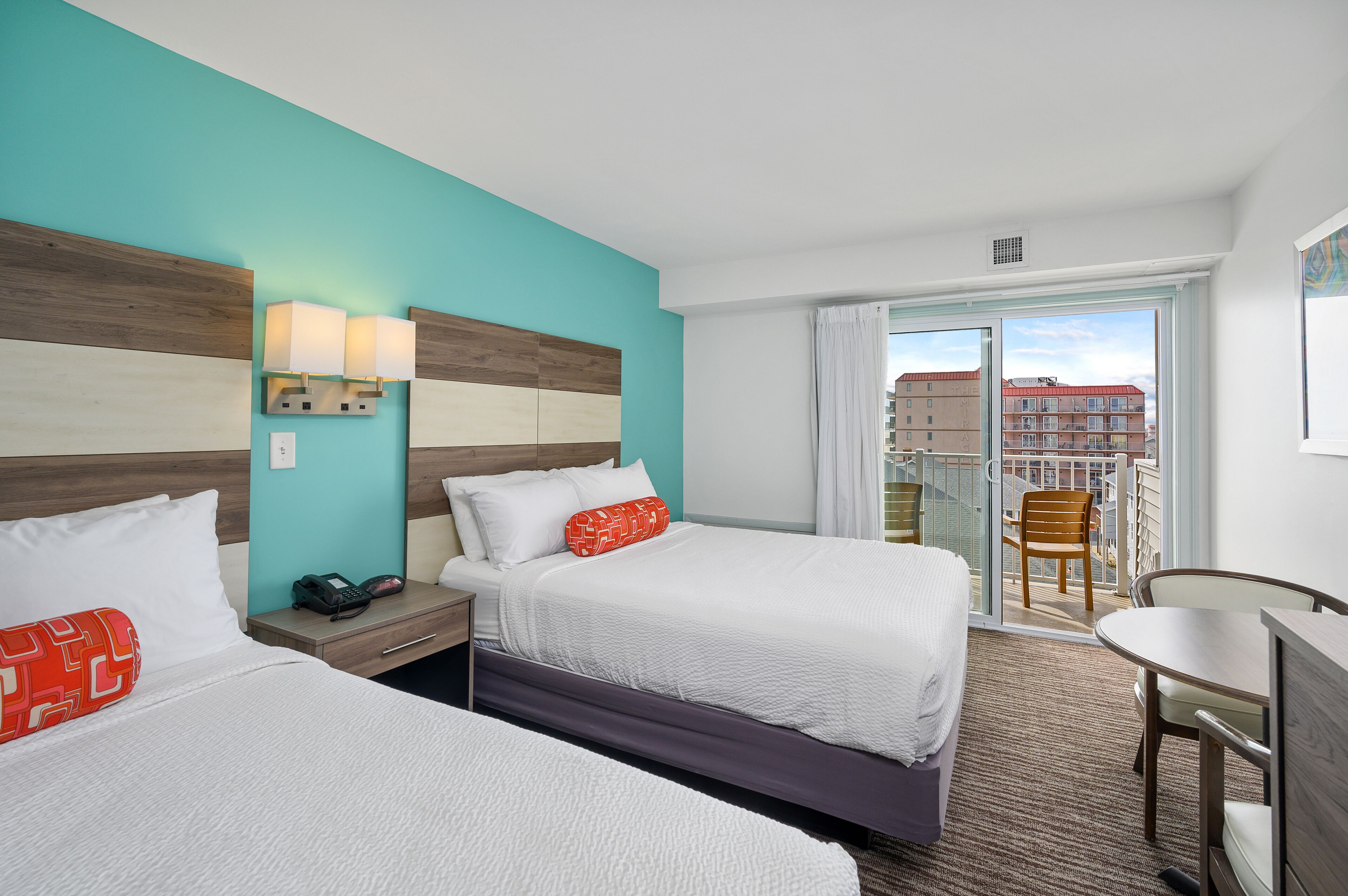 Een hotelkamer met twee bedden, een bureau en een balkon met uitzicht op de stad.