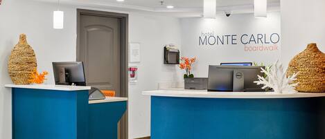 A hotel reception desk with a modern design, featuring two reception counters, a digital screen, and a sign that reads "hotel Monte Carlo boardwalk".