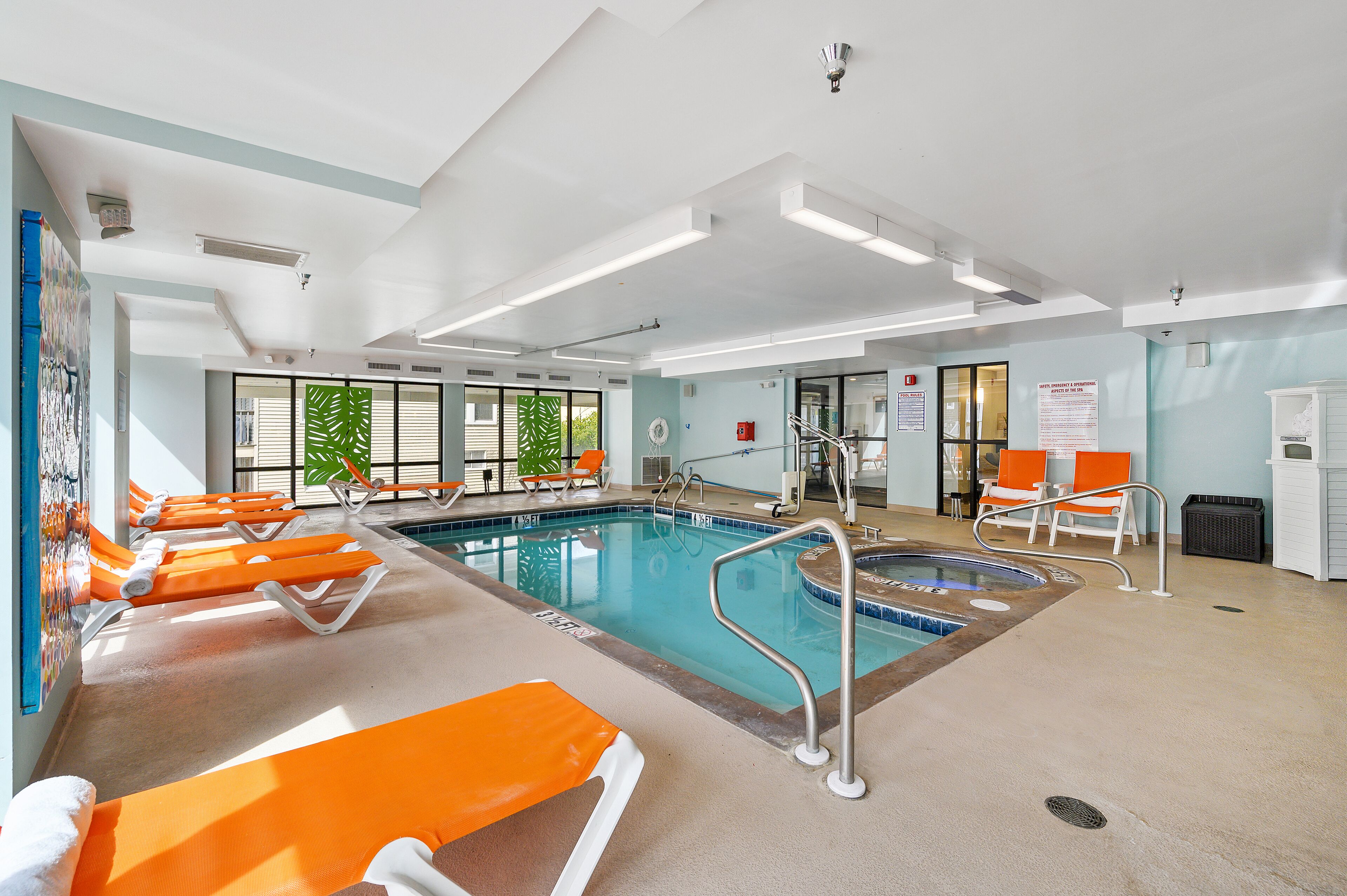 An indoor swimming pool with multiple lanes, lounge chairs, and a changing room.