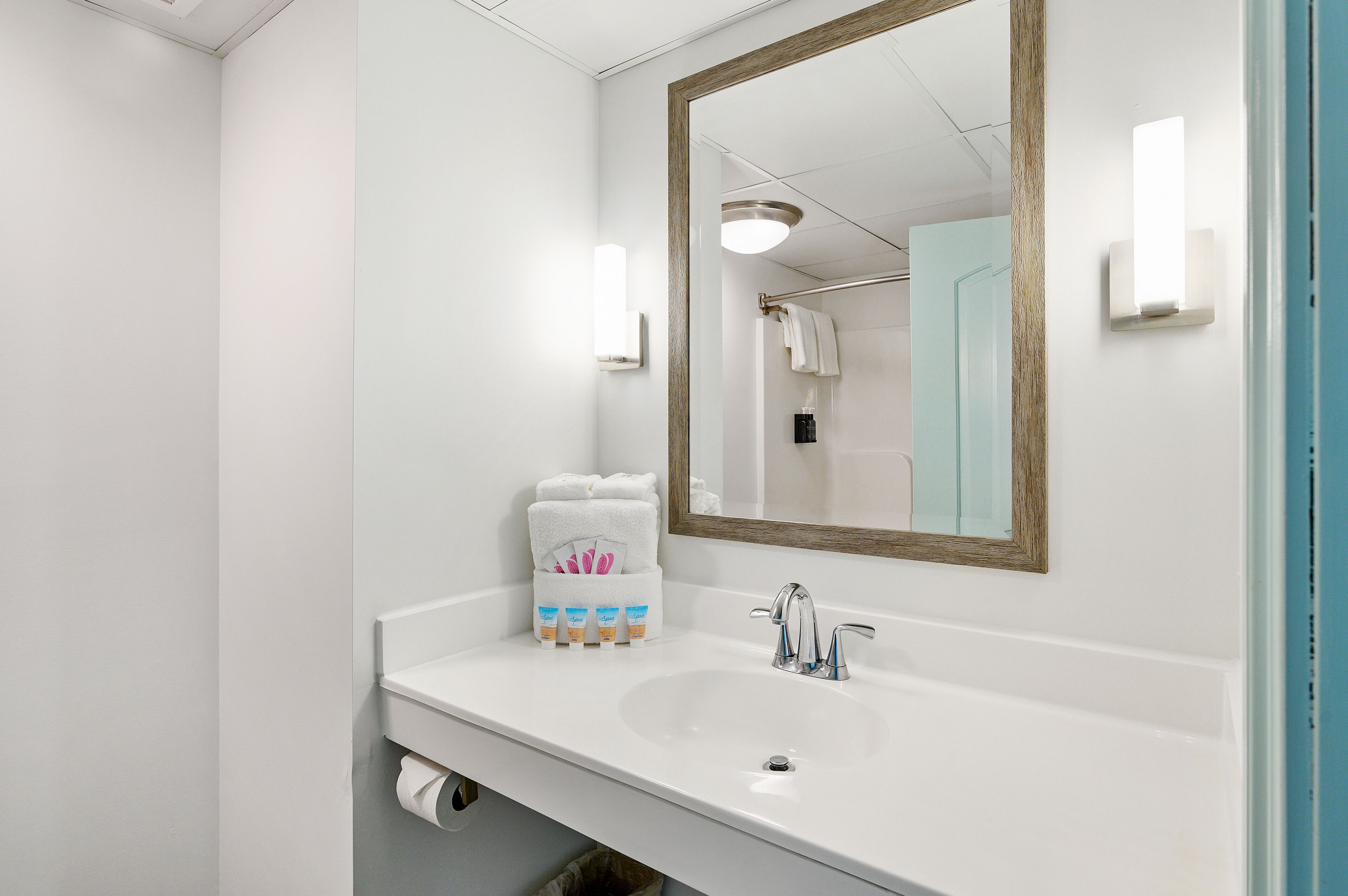 A bathroom with a white sink, a mirror, and a towel rack with towels and toiletries.