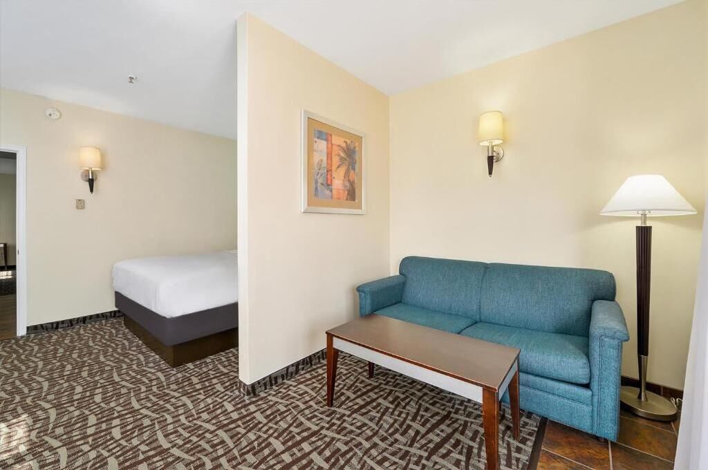 A hotel room with a bed, a blue sofa, a small table, and two wall-mounted lamps.