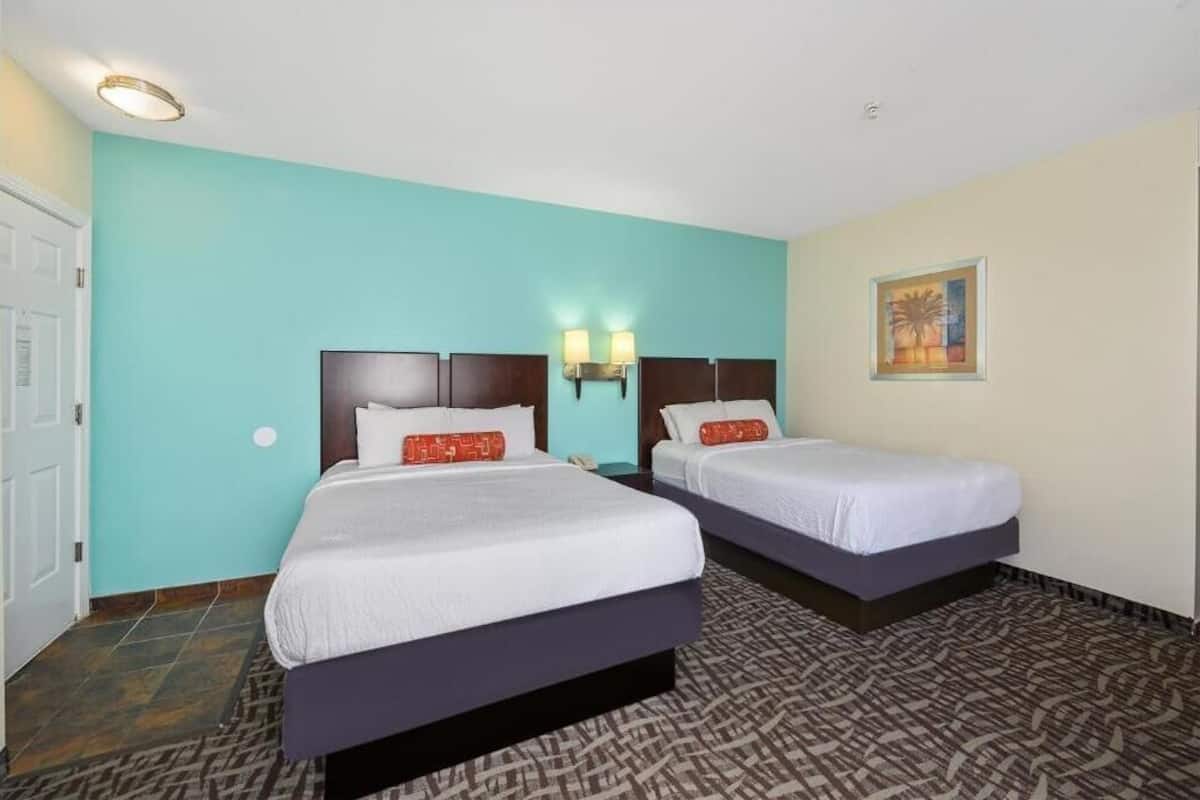 Une chambre d’hôtel avec deux lits, une moquette à motifs, des murs de couleur turquoise et un tableau accroché au mur.