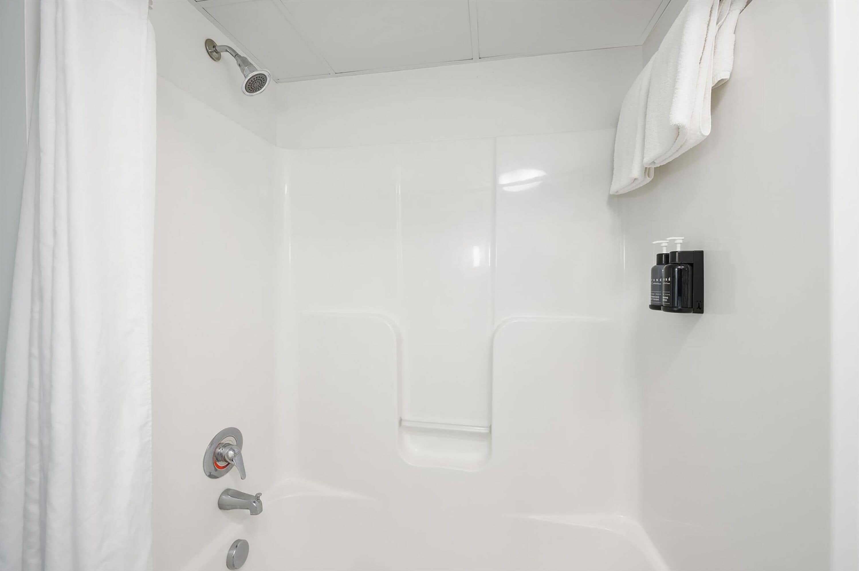 Une cabine de douche blanche équipée d’un pommeau de douche à main, d’un distributeur de savon fixé au mur et d’une serviette accrochée au mur.