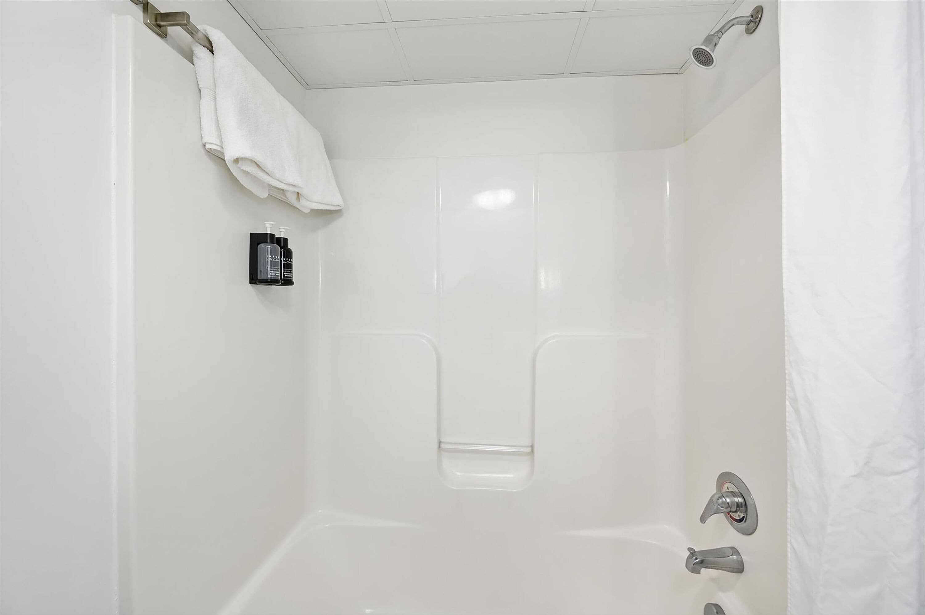 A white bathroom with a shower, a towel rack, and a small shelf with toiletries.