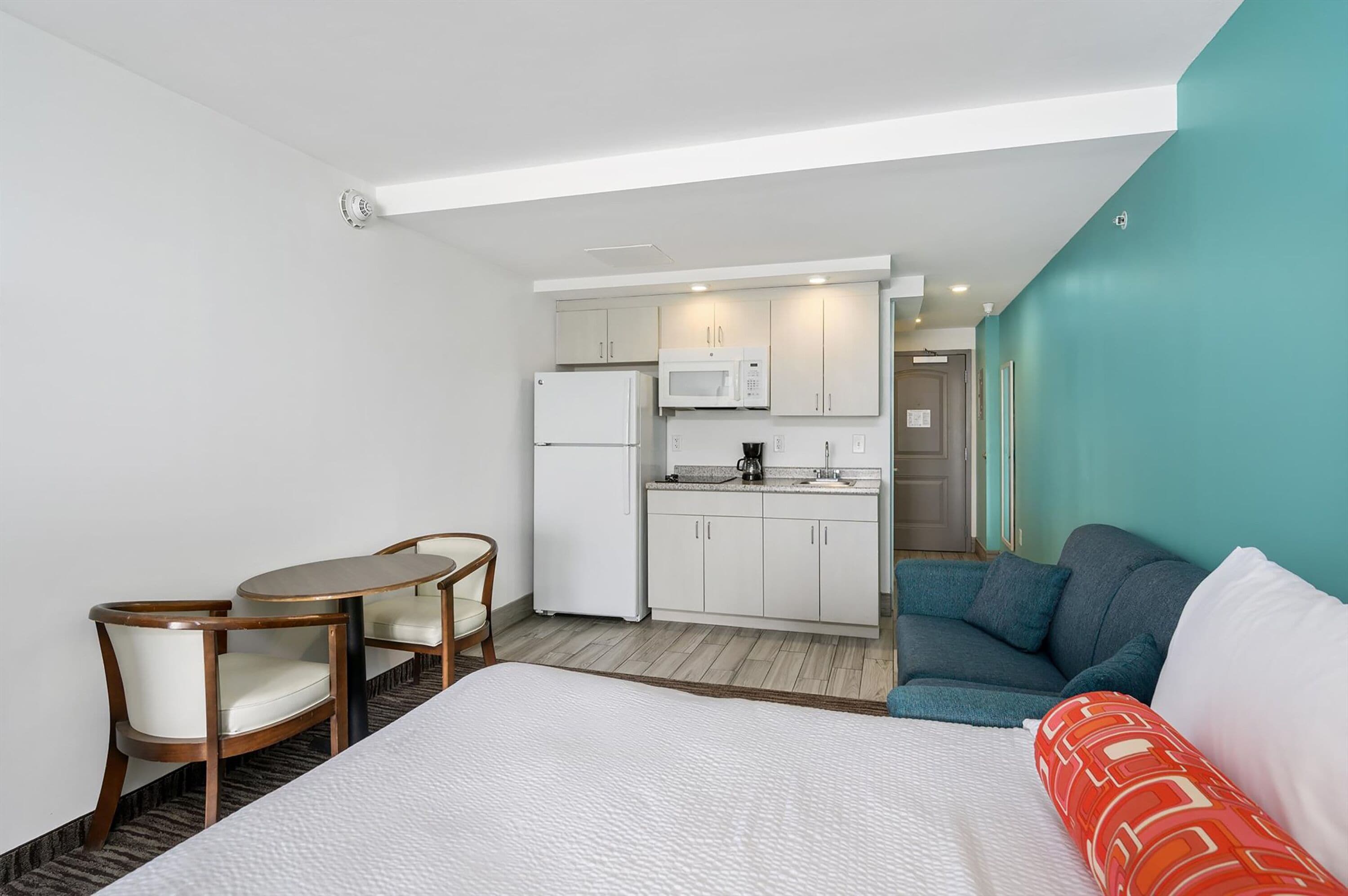 Habitación de hotel pequeña con cama, una mesa de comedor con sillas, una kitchenette con microondas y refrigerador, además de un sofá.