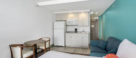 Habitación de hotel pequeña con cama, una mesa de comedor con sillas, una kitchenette con microondas y refrigerador, además de un sofá.