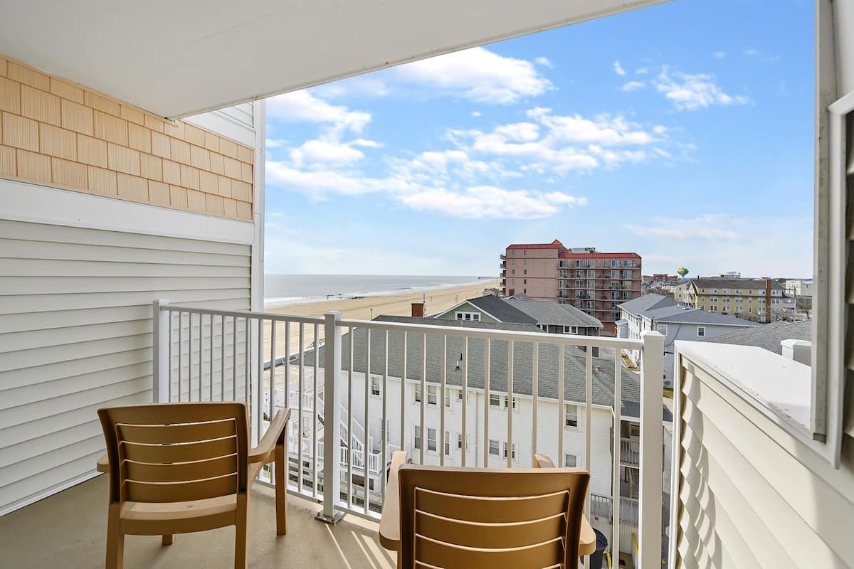 Un balcon avec deux chaises et une table, donnant sur une plage et des immeubles.