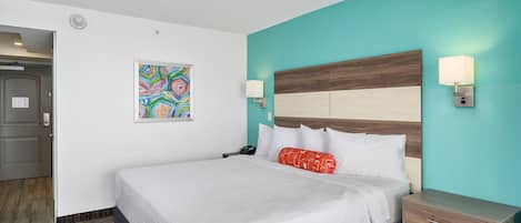 Ein Hotelzimmer mit einem großen Bett, einem Nachttisch, einer Wandlampe und einem farbenfrohen, abstrakten Gemälde.