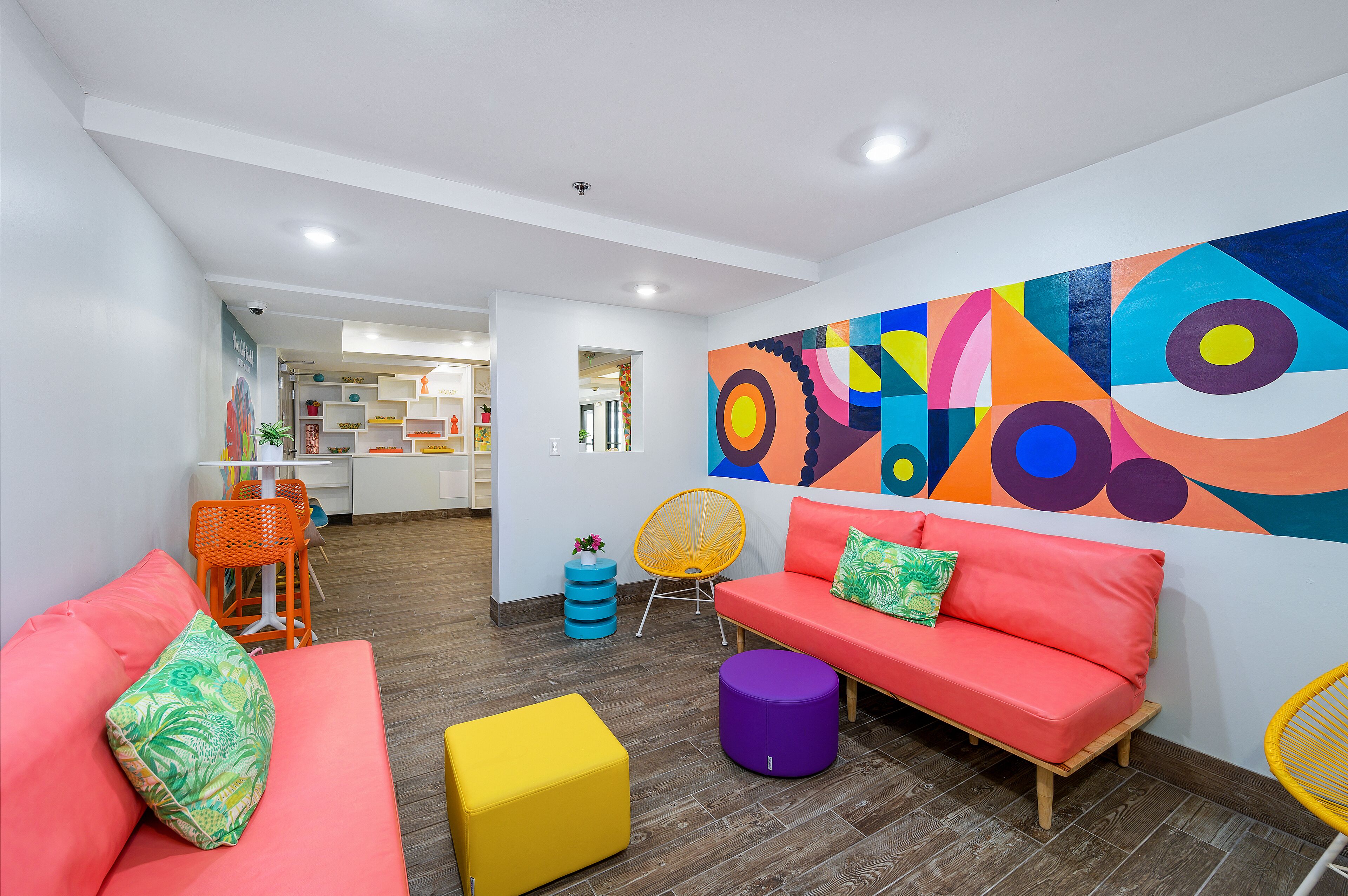 A modern living area with a vibrant abstract mural, a red sofa, a yellow ottoman, and a wooden coffee table.