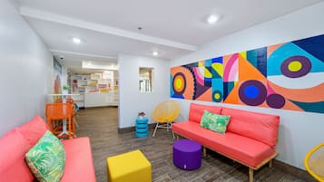 A modern living area with a vibrant abstract mural, a red sofa, a yellow ottoman, and a wooden coffee table.