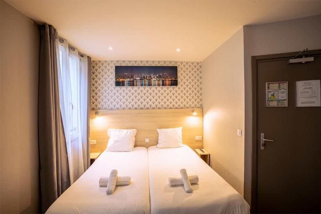 A hotel room with two beds, a cityscape painting above the headboard, and a door with a bulletin board.