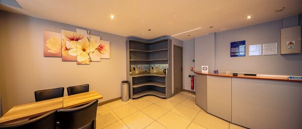 A hotel reception area with a wooden reception desk, a trash bin, and a fire extinguisher. - Hôtel Aix Europe (Paris)